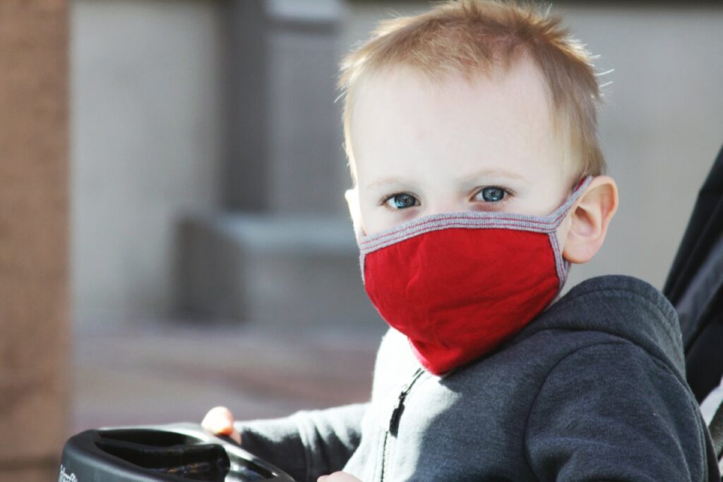 Toddler putting on a red face mask