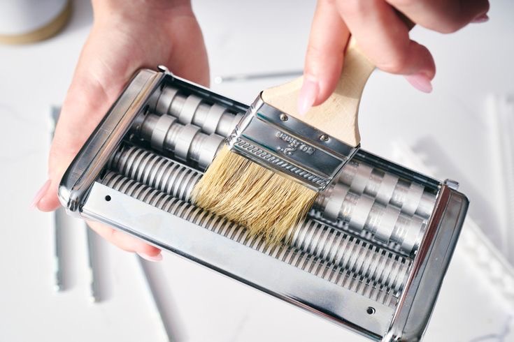 Person cleaning pasta machine with a brush