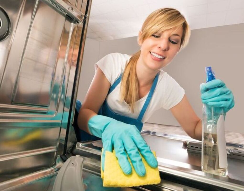 A woman wiping down the interior of her dishwasher