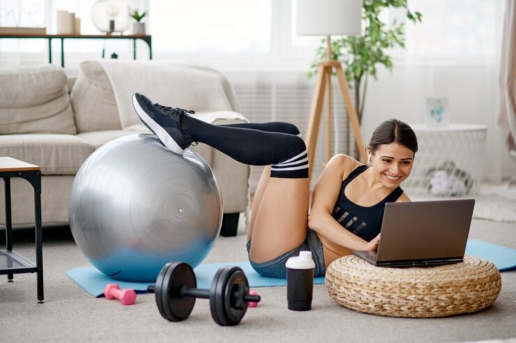 Girl doing exercise with ball, online pilates training at the laptop