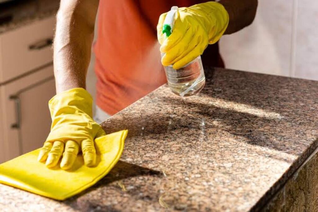 A man cleaning a granite countertop with an unlabelled solvent