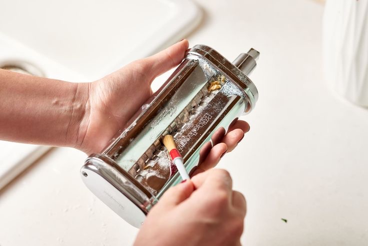 Person cleaning pasta machine with a toothpick