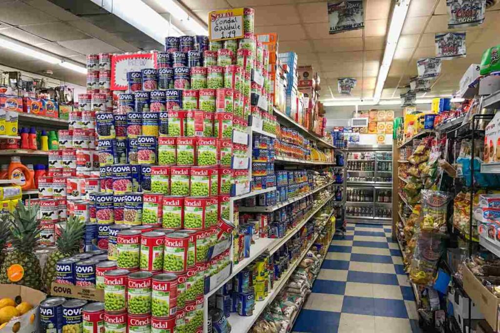 Canned beans and bags of rice line an aisle at a supermarket 