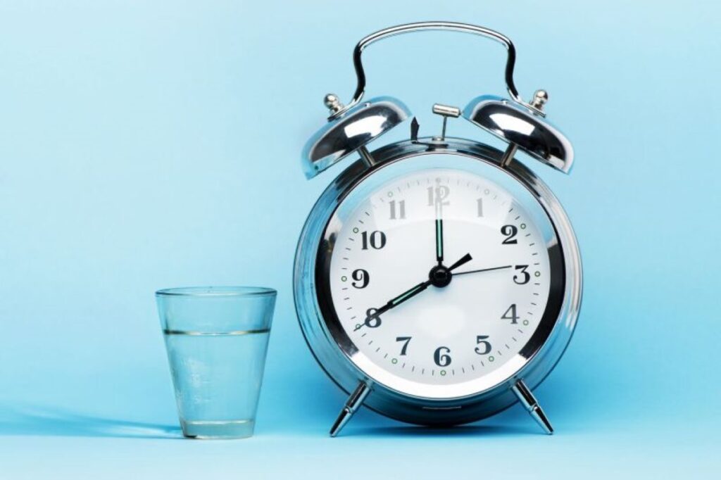 A glass of water next to an alarm clock