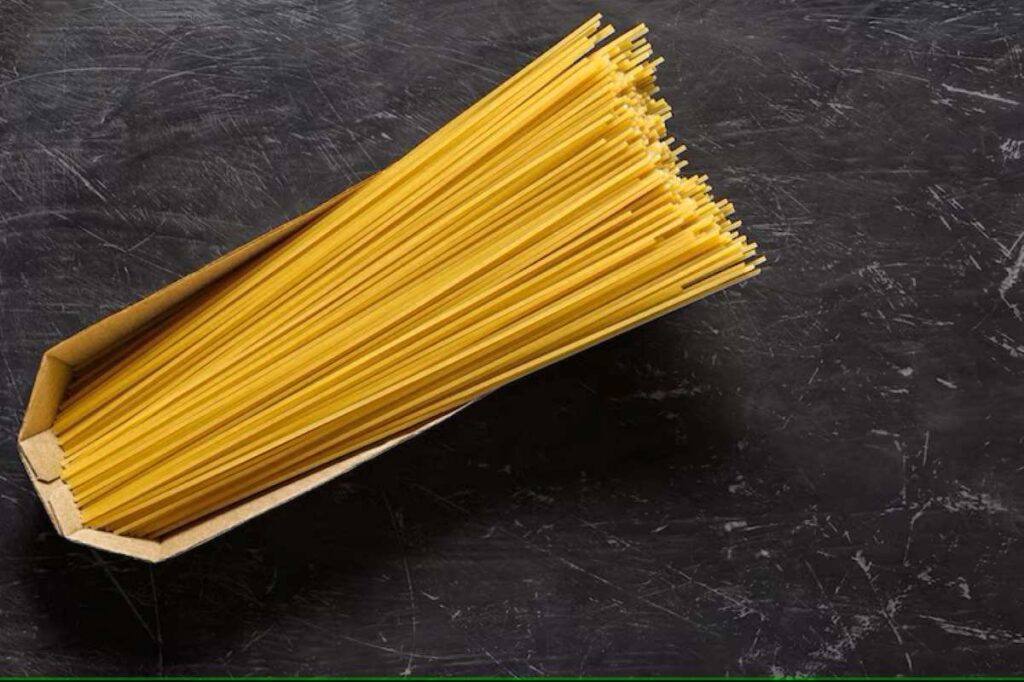 Spaghetti raw, long pasta in cardboard box, top view dark background